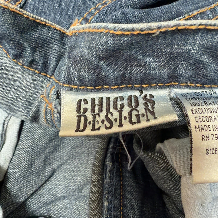 Tag view of blue denim jeans showing embroidered floral hem detail and relaxed straight-leg fit