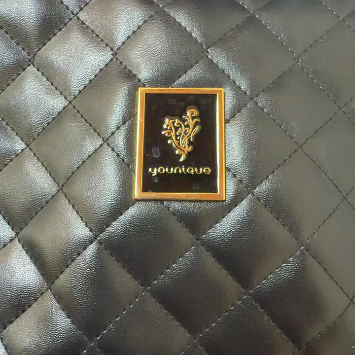 Black quilted crossbody bag worn on shoulder, showing side profile and adjustable gold chain strap