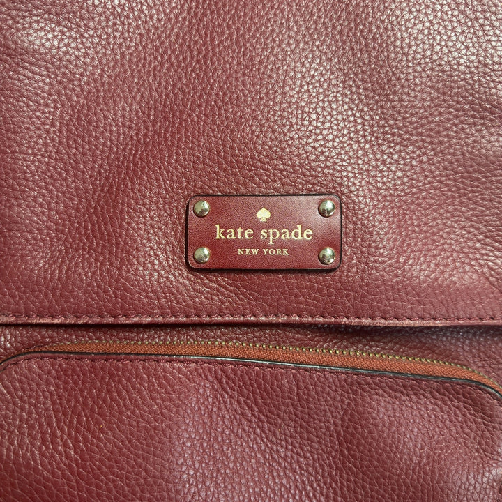 Burgundy leather Kate Spade backpack worn on shoulders, showing back view with adjustable straps and structured design