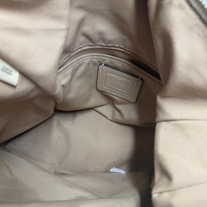 Tag view of cream Coach crossbody bag with black leather strap worn across body