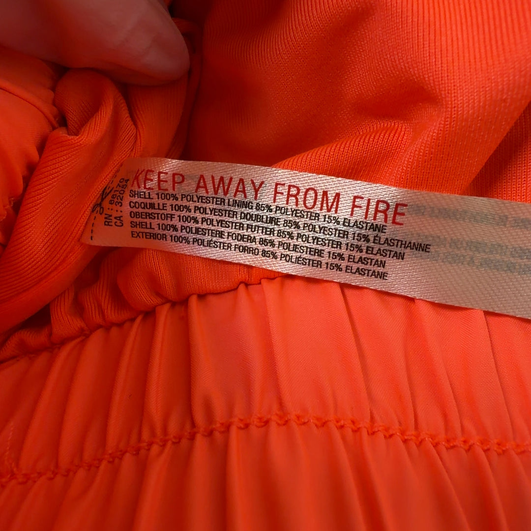 Woman wearing orange ruched athletic shorts with black sports bra, back view showing flared silhouette
