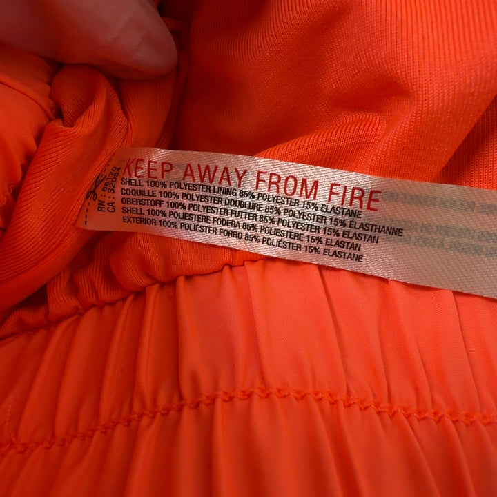 Woman wearing orange ruched athletic shorts with black sports bra, back view showing flared silhouette