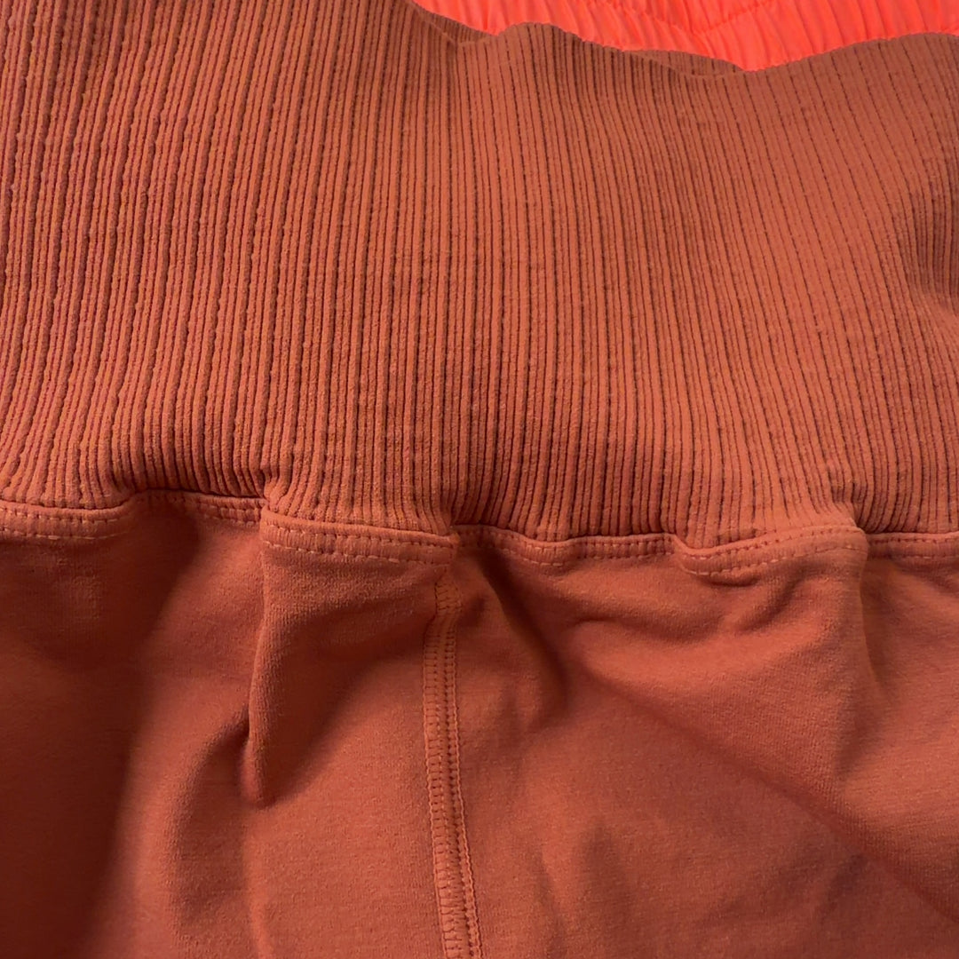 Woman wearing orange ribbed high-waist activewear shorts with black sports bra, side view showing fit