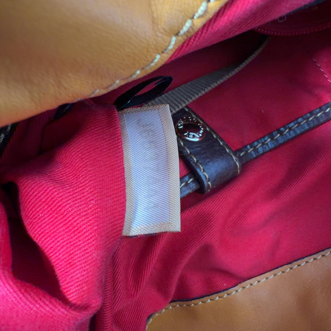 Tag view of orange leather Dooney & Bourke hobo tote bag worn on shoulder, showing structured silhouette and brown leather details
