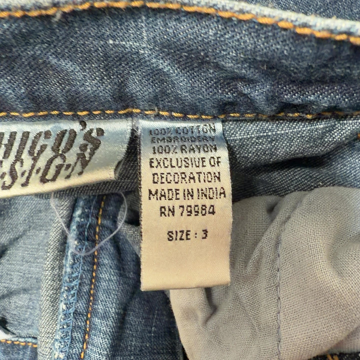 Tag view of blue denim jeans showing embroidered floral hem detail and relaxed straight-leg fit