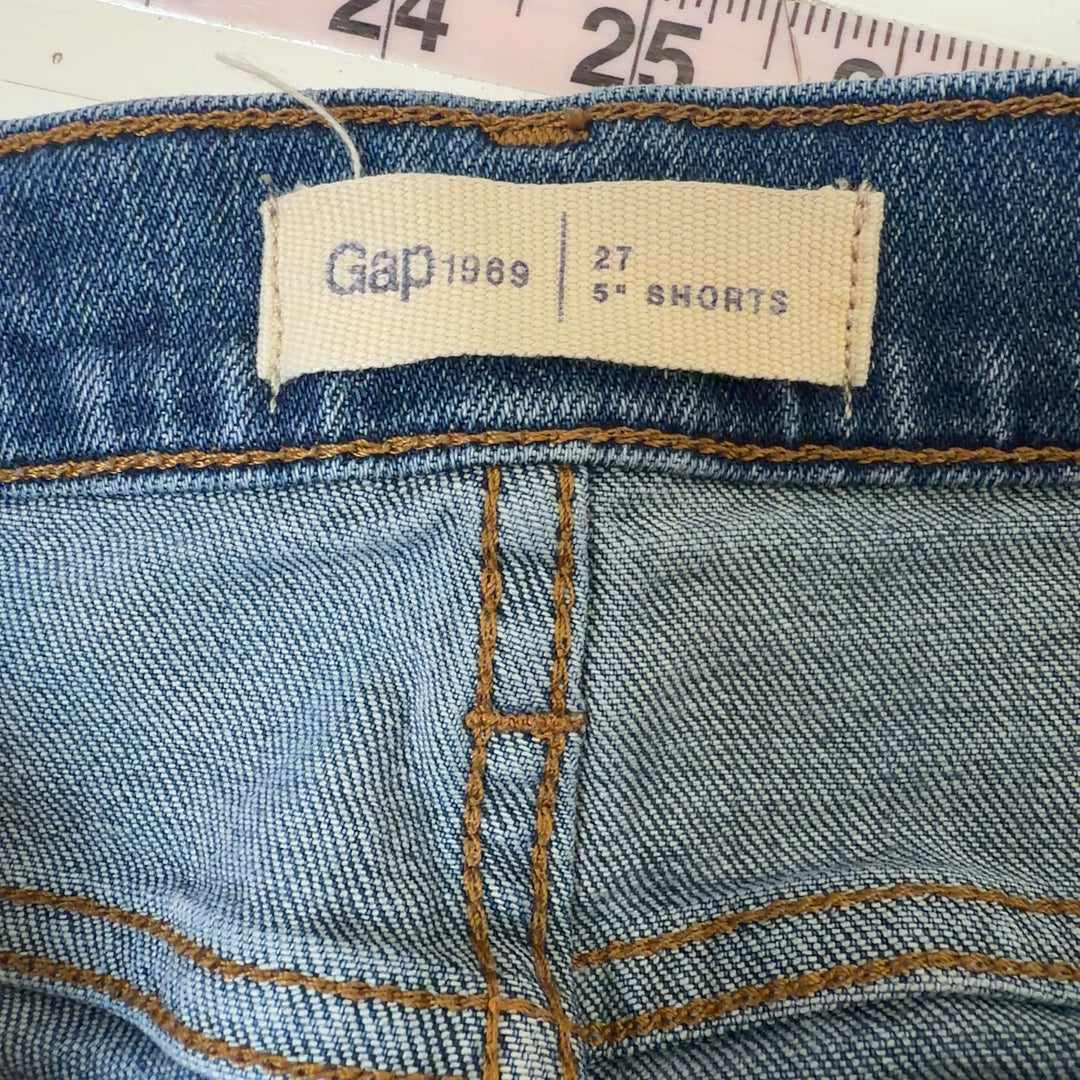 Tag view of blue denim shorts showing distressed rip detail on thigh and classic denim construction