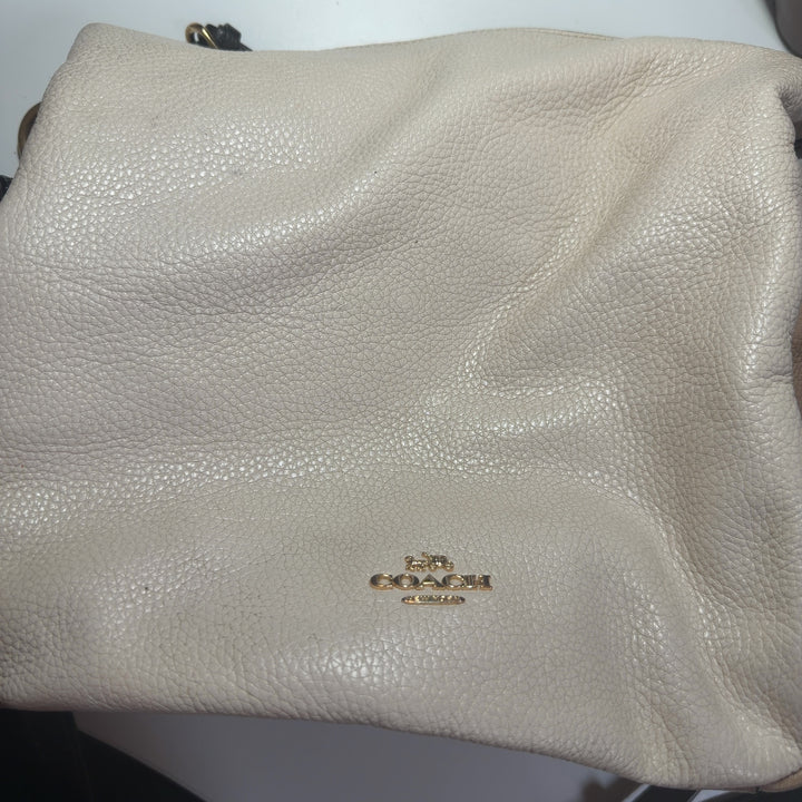 Tag view of cream Coach crossbody bag with black leather strap worn across body