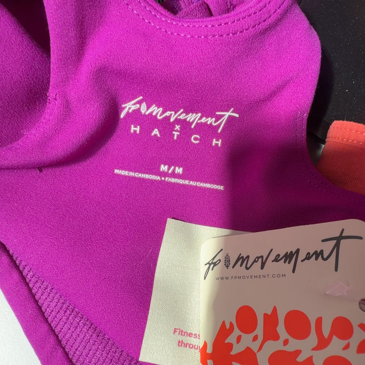 Woman wearing magenta sports bra with black leggings, back view showing crop top design