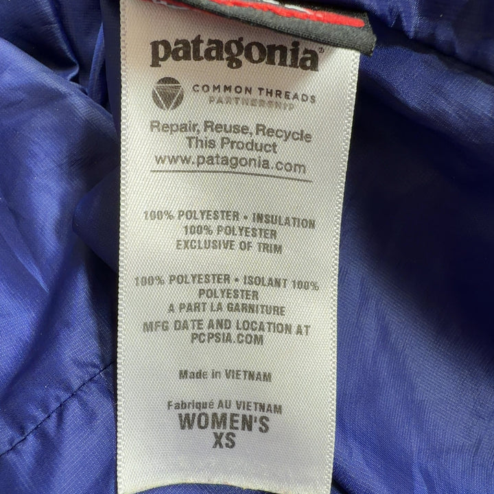 Tag view of turquoise quilted Patagonia puffer jacket with navy hood lining on woman