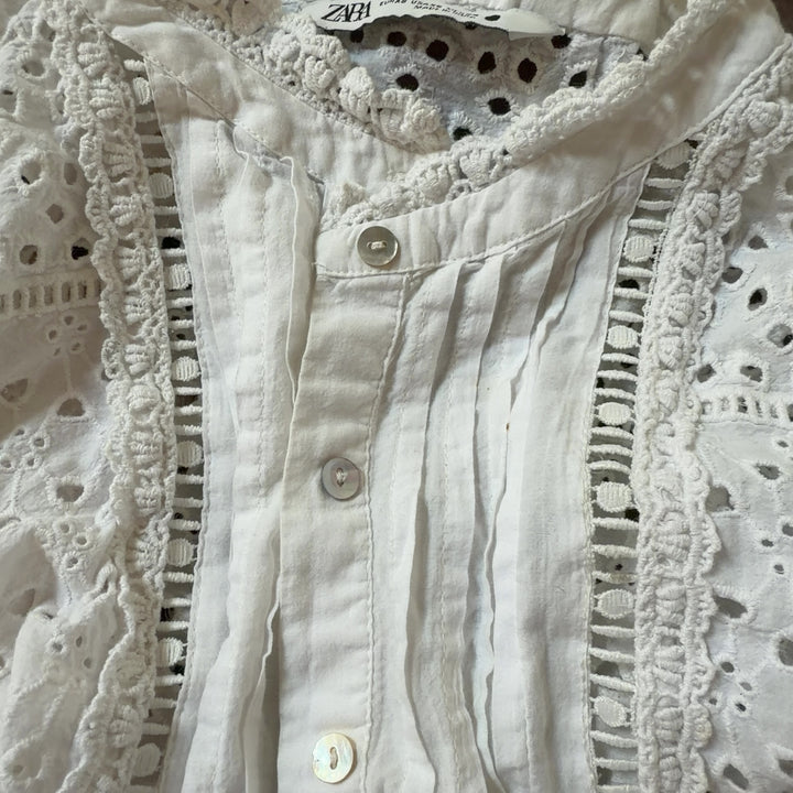 Tag view of cream eyelet cropped top showing lace pattern and pleated design